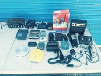 Overall view of all electronics items on table including amplifier, microphones, portable players, remotes, and accessories.