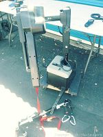 Full view of the wheelchair lift mechanism with arm extended, red strap, and mounting hardware laid out on the ground.
