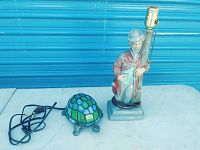 Photo showing both lamps: the turtle lamp with stained glass shell and the figurine lamp of a man leaning on a street light.