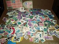 Wide assortment of postage stamps in loose pile showing different colors and designs including some attached in strips or blocks