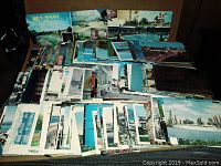 Overview photo showing a large spread of used postcards, stacked with a variety of scenes visible including city skylines, landmarks, and scenic views.