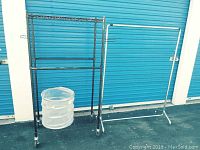Metal clothing rack with caster wheels and laundry drying rack in front of blue garage door.