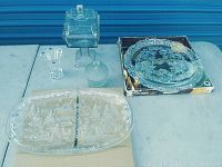 Photo showing Carmen round platter, holiday oval platter, two candy dishes with lids, and frosted glass jar on table outdoors
