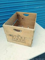 Top-front angle view of the wooden crate showing the Whole Foods logo on one side and cutout handle on the opposite side.