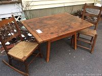 Photo showing antique wooden low rectangular table with two child-size wooden chairs placed on pavement outside. Table top surface shows wear and marks.