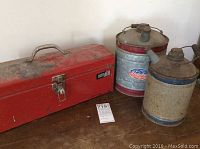 Photo of a closed red vintage metal toolbox and two metal gas cans showing condition and size