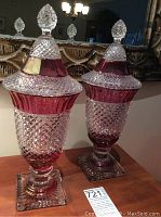 Pair of vintage large cranberry flash candy jars with lids, diamond cut pattern, on a wooden surface under chandelier light