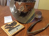 Photo showing the futuristic designed silver-toned Hennessy ice bucket, coaster, tongs, and glass bottle stopper on a wood table.