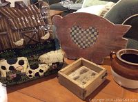 Wooden pig-shaped cutting board, glazed ceramic pot, vintage farm-themed pressed metal letter holder decorated with cows and chickens, and old butter mold box.