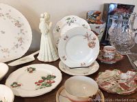 Group photo showing vintage porcelain plates, cup and saucers with floral patterns, porcelain angel figurine, Asian-style vase, and crystal pitcher.
