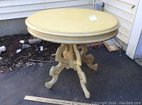 Full view of vintage small round table in dark cream color with gold accents, showing round top and pedestal base with curved legs on casters.