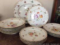 Full dish set on dark wood surface showing 15 pieces with floral hand painted decoration and gold trim.