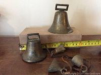 Photo showing all five brass bells of varying sizes with measuring tape indicating size of about 3.5 inches for largest bell