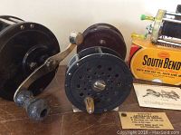 Four vintage fishing reels shown including South Bend reel with box and manual, Penn No.97 Deep Sea reel and two fly fishing reels, all on a wooden surface.