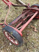 Close-up of the red rotary mower's wheel and blade mechanism showing metal blades and wheels with some rust.