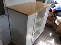 Full view of the white cabinet island showing the wood countertop and cabinet doors with knobs on one side and smooth doors on the other side.