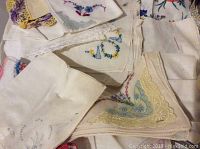 Close-up showing various white and cream handkerchiefs with colorful floral embroidery and lace edges.