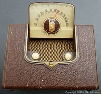 Front view of radio with dial up showing radio dial, Royalty of Radio emblem, grille speaker area, and two white knobs in brown textured faux leather case