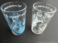 Photo showing the two Flintstones golf themed juice glasses from a side angle, highlighting the printed characters and text.