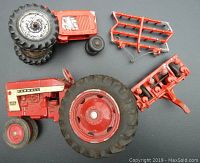 Photo showing the Farmall IH 404 tractor, the unbranded tractor, and two red farming attachments laid out on a flat surface.