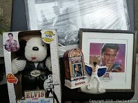 Lot display showing multiple Elvis Presley collectibles including framed art, plush dog in black leather, an Elvis Jukebox Stein, and figurine