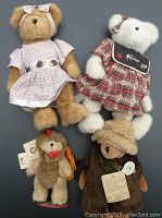 Front view of four plush bears: two dressed in purple gingham dresses (one tan, one light brown), one white dressed in red plaid dress with tag, and a small turkey bear on a stand with its tag visible.