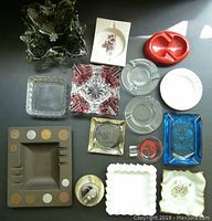 Top-down view showing various ashtrays arranged on a black surface including cranberry & clear cut glass, green ornate glass, clear and colored glass, ceramic and promotional Marlboro ashtrays