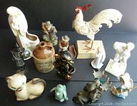 Collection of assorted figurines and collectibles including metal rooster sculpture, whisky jug, Haeger planter, animal and character figurines on black background
