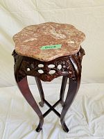 Front-side angle of wooden pedestal stand showing carved apron and scalloped faux marble top.