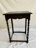 Side view showing the carved apron, turned legs, and rectangular stretcher base of the dark wood side table.