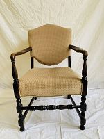 Front view of beige upholstered wing chair with dark wooden frame and carved legs.