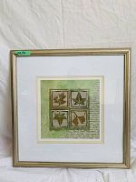Front view of framed art piece showing four green botanical leaves and script writing in a 22x22 inch light gold frame.