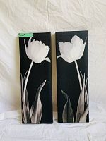 Two vertically oriented rectangular canvases with black and white images of tulip flowers and leaves on a solid black background.