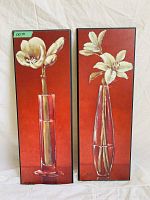 Photo showing two framed vertical paintings of white flowers in red vases against a red background.