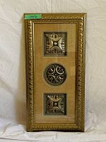 Photo shows framed art with three metal medallions mounted vertically on beige matting inside a decorative gold frame.