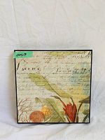 Photo of square wall art depicting flowers, leaves, shells with vintage writing in background.