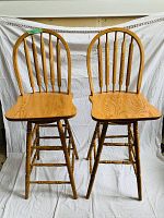 Front view of two wooden bar stools showing the spindle backrest and contoured seat details