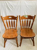 Photo showing two wooden kitchen chairs with spindle backs and turned legs placed side by side against a white backdrop.