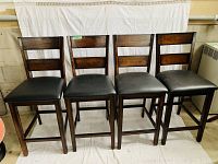 Front view of four bar stools aligned, showing wood ladder-back and padded black seats