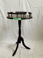 Side view of wooden side table showing circular top with curved guardrail and turned pedestal base with three legs.