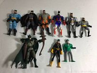 Nine Batman-themed action figures arranged on a flat surface; various costume designs and accessories visible.