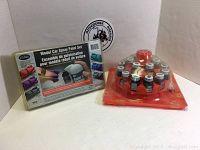 Two unopened Testors paint sets on white surface: one boxed spray paint set with model car image and one clear circular paint bottle set in plastic packaging.