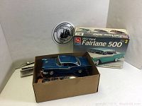 Three model cars inside and on top of a cardboard box, including a blue 1957 Ford Fairlane 500 with its original box visible in the background.
