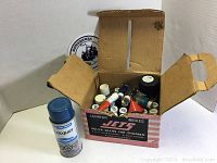 Cardboard box with various small bottles of Testors model paints and a spray lacquer bottle shown outside the box.