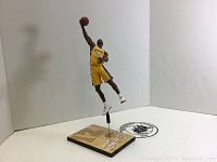 View of Dwight Howard figure posed in air holding basketball, showing Los Angeles Lakers yellow jersey number 12 and black support rod attaching figure to base.