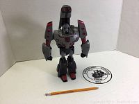 Gray and red Transformers Megatron figure standing on a white surface with a pencil for size reference.