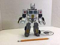 White and gray Transformers Optimus Prime action figure in robot mode, shown with pencil for scale.