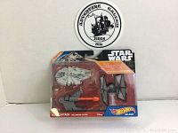 Unopened Hot Wheels Star Wars Blast Attack blister pack containing the Millennium Falcon and TIE Fighter die-cast models, with packaging showing Star Wars and Hot Wheels branding and colorful design.
