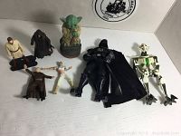 Overall lot showing 7 Star Wars loose figures including a vintage 1980 Yoda, Darth Vader, General Grievous, others.