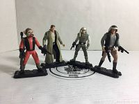 Four Kenner Star Wars action figures from left to right: Rebel Pilot, Luke Skywalker, Rebel Soldier, Han Solo, each with black display stands and original weapons.